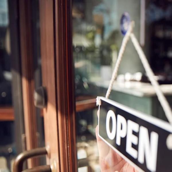 women looking at 'open' sign through window of business