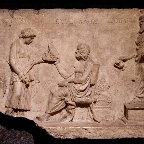 a marble bas-relief showing Euripides (seated), a woman holding out a theater mask to him and the god Dionysus