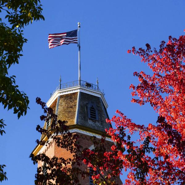 Flag flying atop Old Main building framed in red autumn leaves
