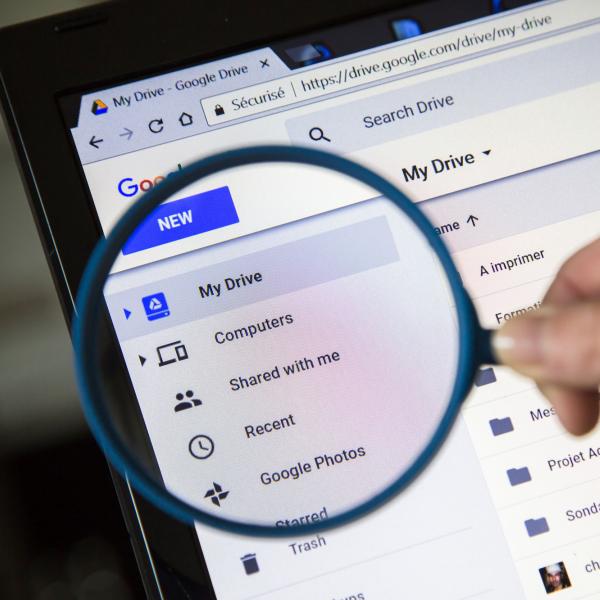 person holding a magnifying glass up to Google Drive screen on laptop