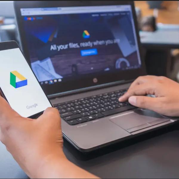 A person holds a cell phone and has a laptop at hand.
