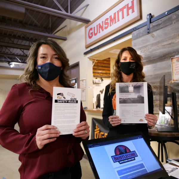 Two women hold up educational materials near a set of cash registers