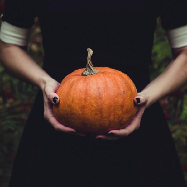 Woman in black dress holds a small orange pumpkin in her hands