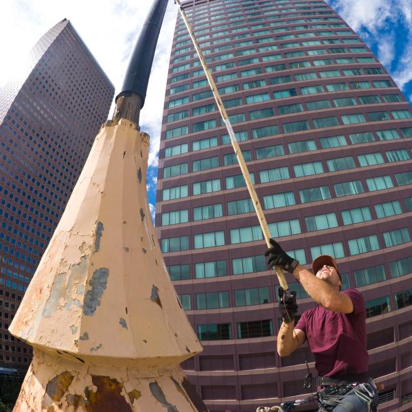 A worker is seen with a long pole, painting a flagpole in downtown Denver.