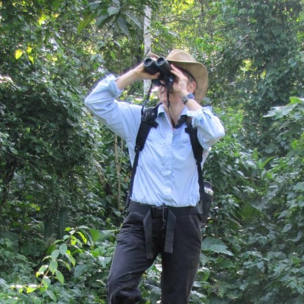 Joanna Lambert standing on tree limb and looking through binoculars.