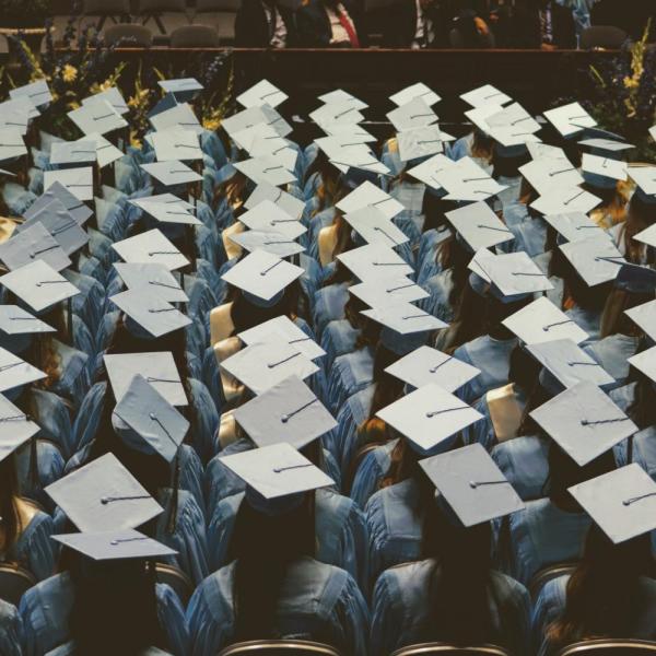 Graduates in caps and gowns sit facing stage at commencement ceremony