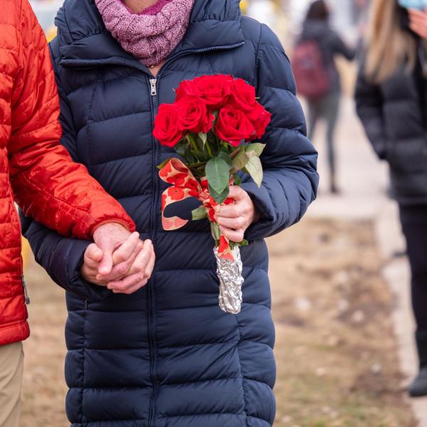Two people, one of them carrying a bouquet of flowers, hold hands.