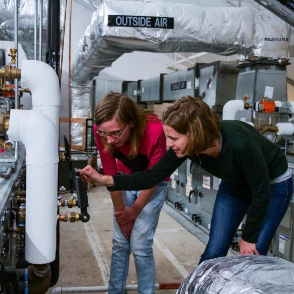 Two students checking the temperature and pressure settings for a rooftop HVAC unit in the Larson Laboratory (Photo via CU Boulder)