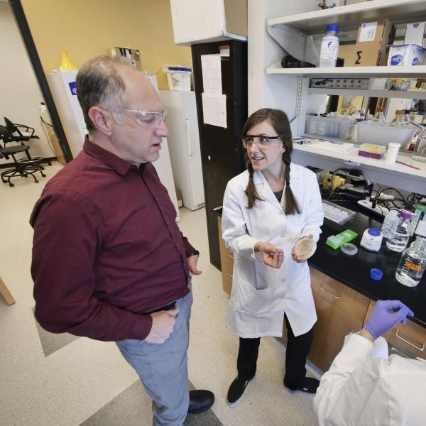 Karl Linden examines a petri dish with students in the lab