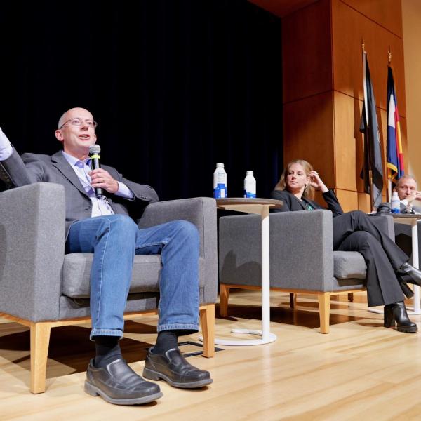 three people sit in chairs on a stage