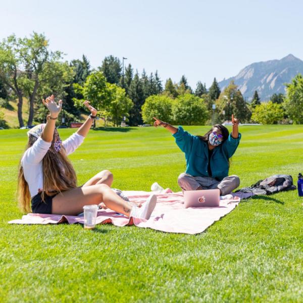 Students in masks sitting on blankets on grass