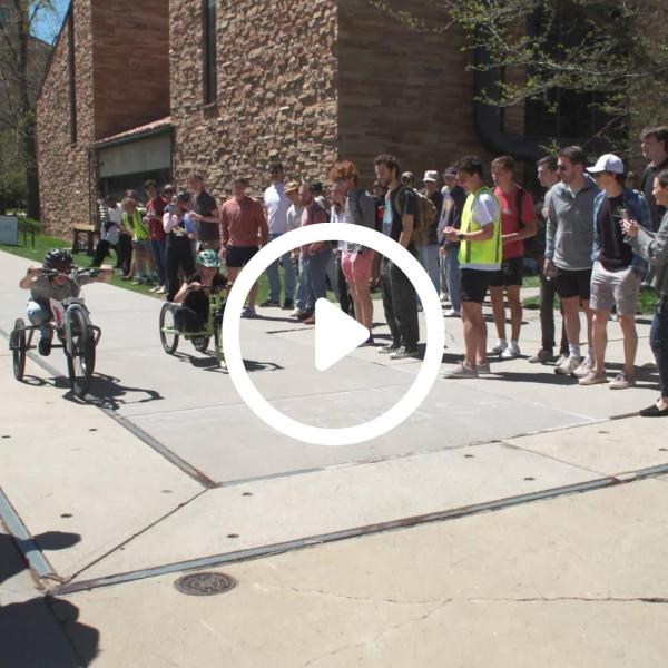 Students competing in an engineering competition with a play button graphic overlay