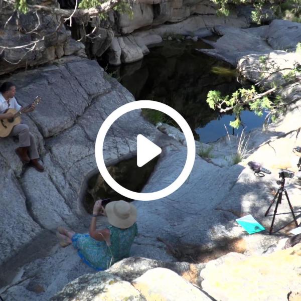 Person sits on rock formation and plays music.