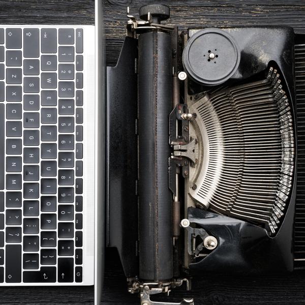 A laptop computer and a typewriter sit back to back