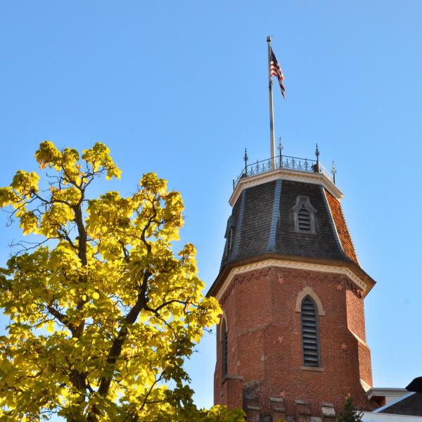 The tower of old main against a blue sky, framed by a branch of yellow leaves.
