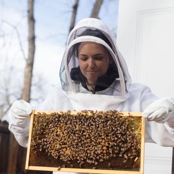 Orit Peleg in a protective suit holds up a tray of bees