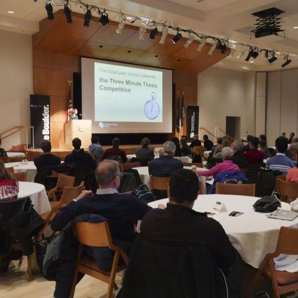 attendees sit at tables watching a past 3MT competition