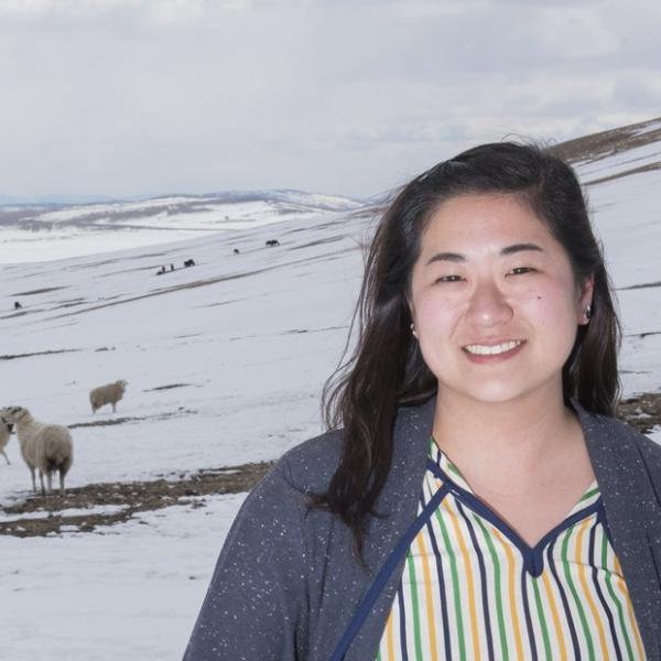 Peace Corps volunteer in front of sheep on snowy hill