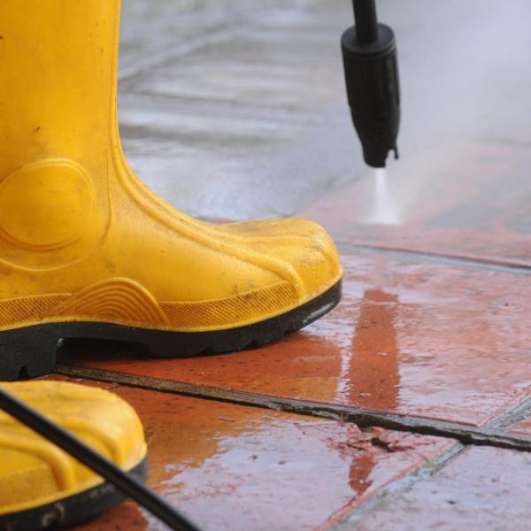 Person wearing yellow rubber boots and power washing the ground