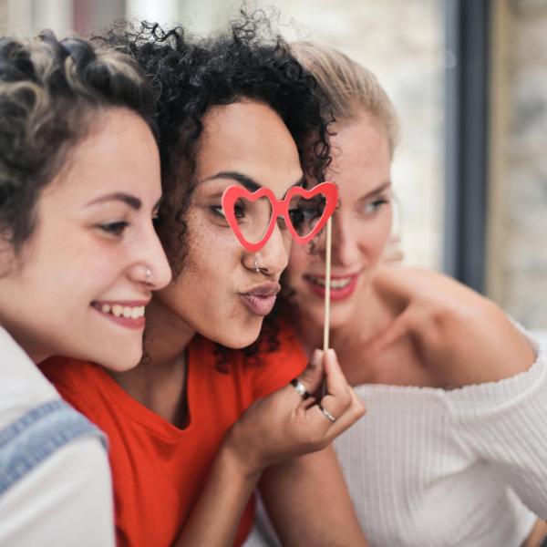 Three friends posing for a photo, one with red heart-shaped glasses