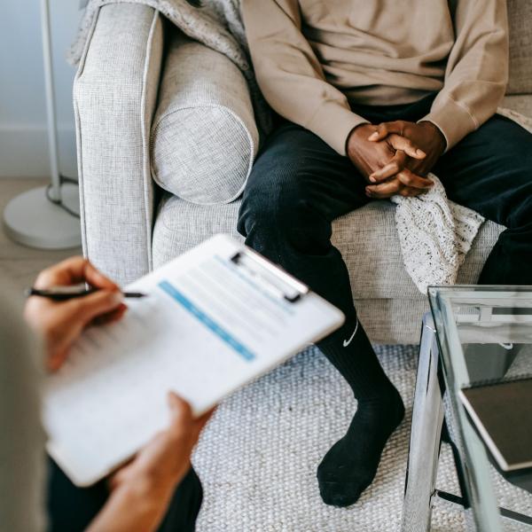 Person sits on couch with someone else holding a clipboard in the foreground