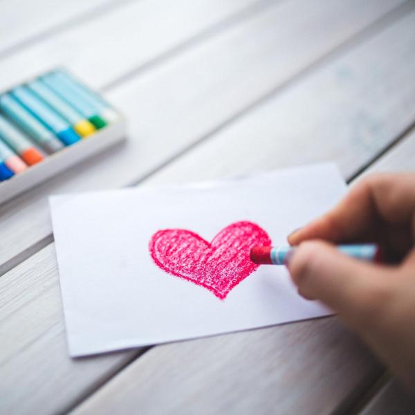person drawing a red heart on a piece of paper