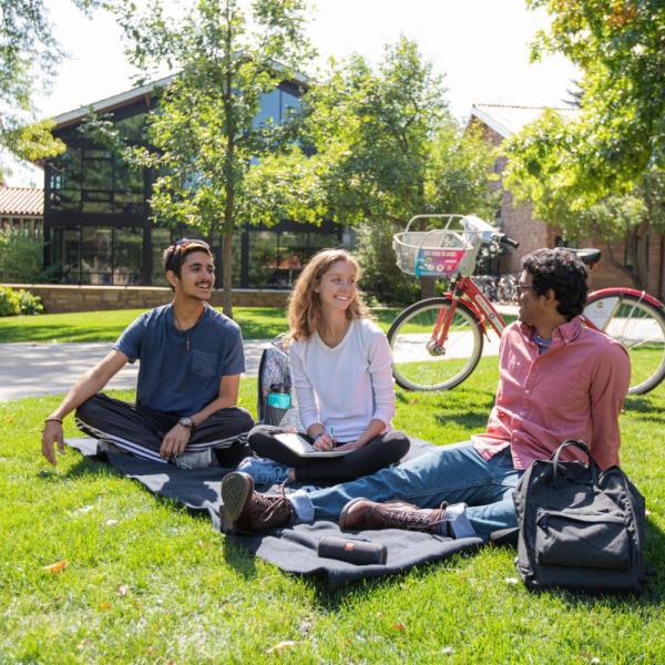 Group of students sitting on the grass at Kittredge Pond smiling