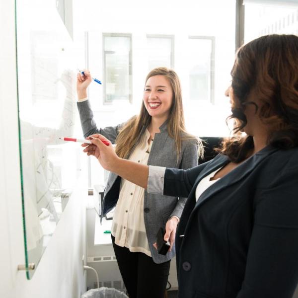 Two professionals write on a whiteboard