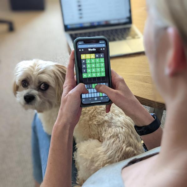 A young woman plays a game of Wordle with a dog on her lap