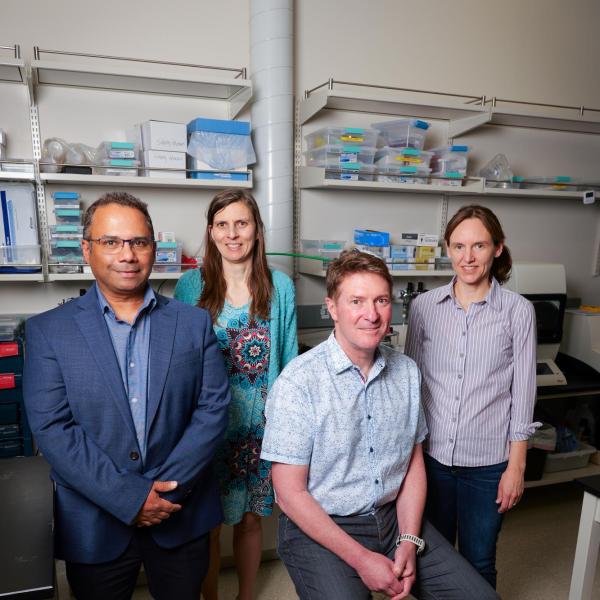 Two women and two men pose for a photo in front of a lab bench