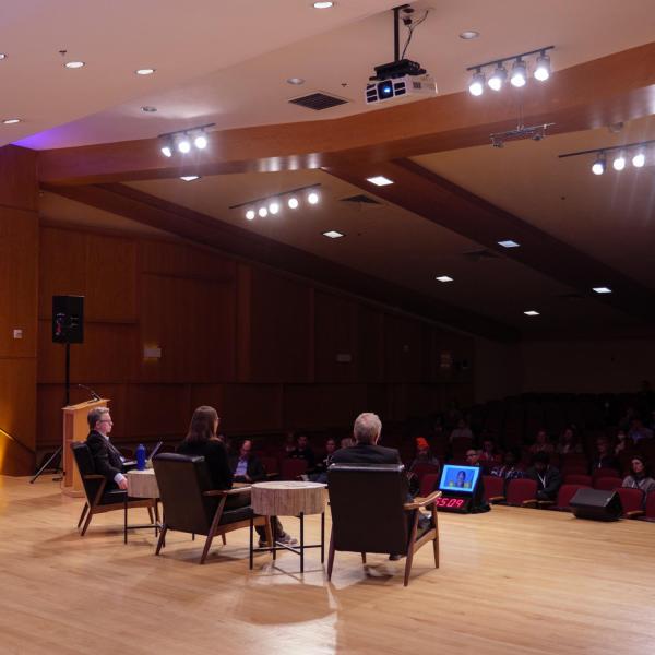 Panelists sit in chairs on stage facing audience members