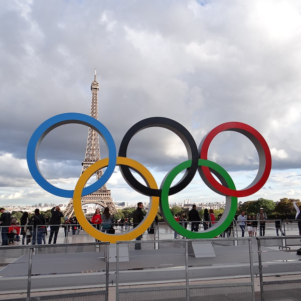 Statue of five Olympic rings in foreground with plaza and Eiffel Tower in the background