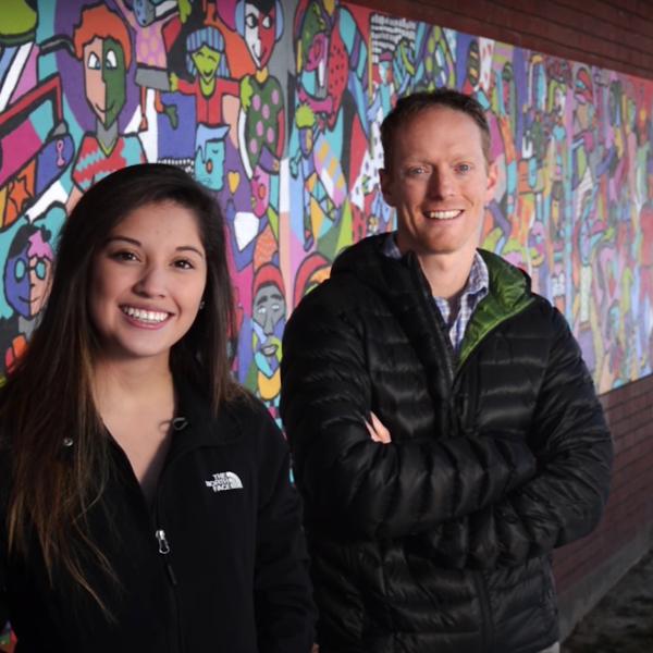 Student with mentor, posing in front of colorful mural