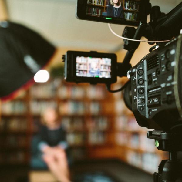 Person sitting, facing a video camera, bookshelves in the backgrounnd. (Sam McGhee/Unsplash)