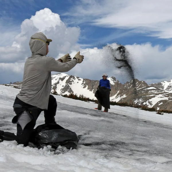 Person throwing black sand while kneeling in the snow on a mountain