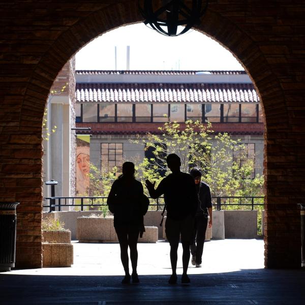 Silhouettes of students walking under archway on campus