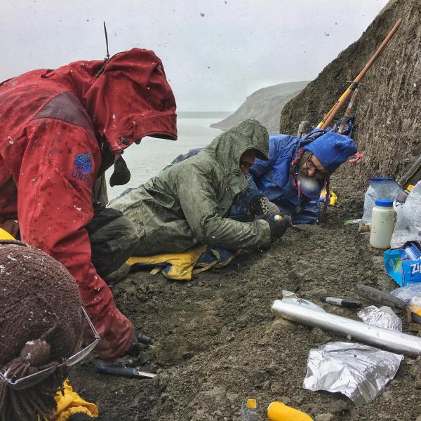 People dig in a long along a riverbank as snow falls