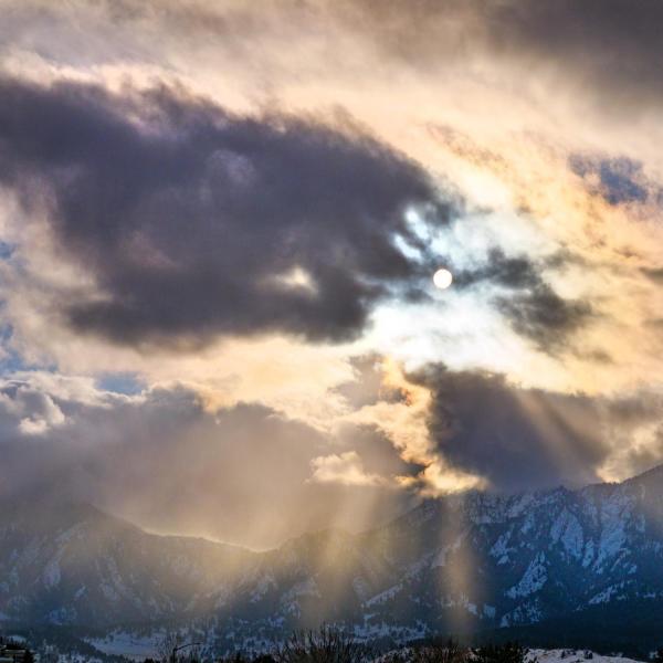 Sun peaks through clouds over snow-covered Flatirons