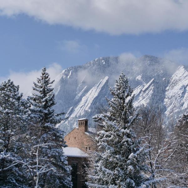 Snowy trees and mountains frame the top of a campus building