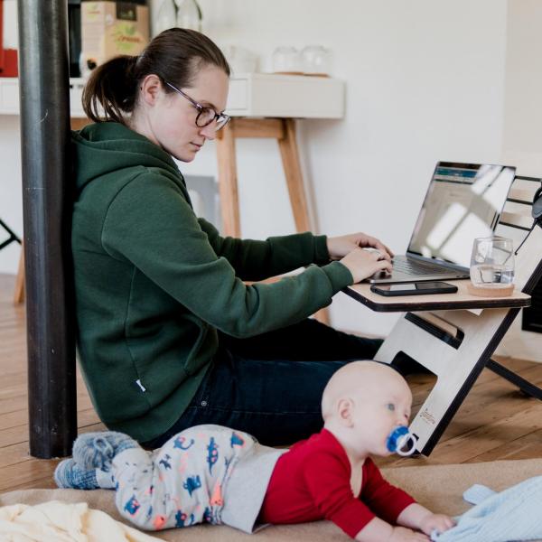 parent working on laptop while baby crawls on floor