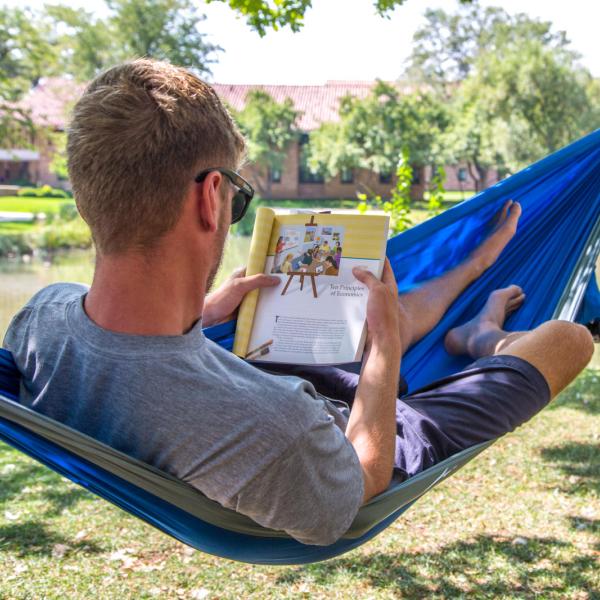 student lounging on a hammock and reading a textbook