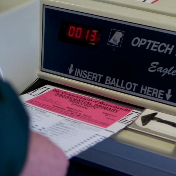 A person slides a ballot into an electronic voting machine.