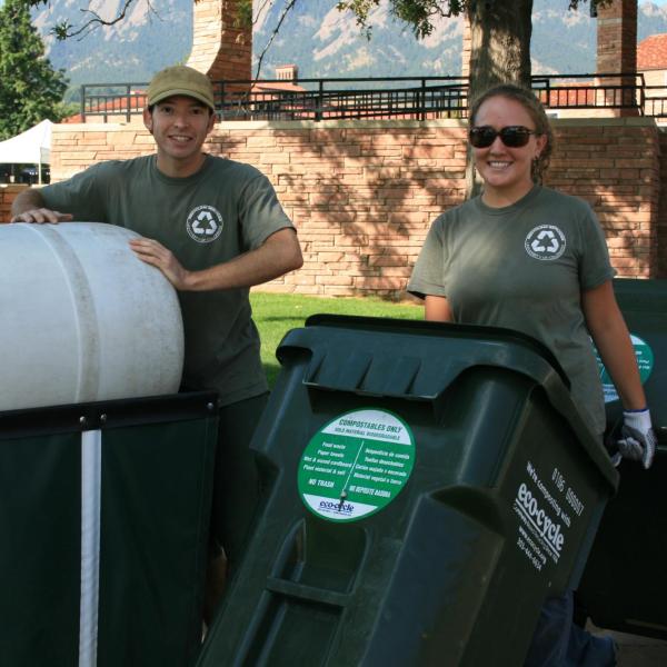 Two people rolling recycling bins on campus