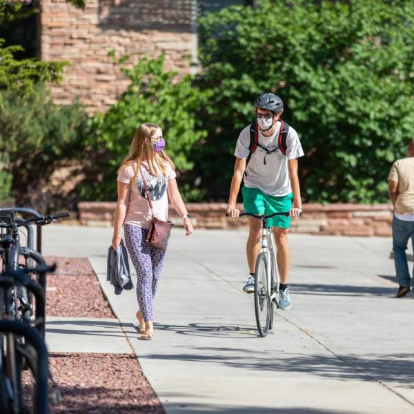 Student riding a bike on campus, while a friend walks alongside him