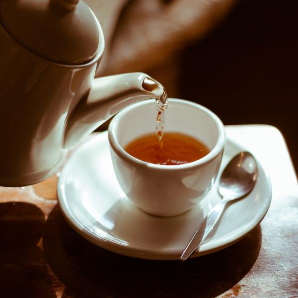 Tea is poured from a white kettle into a white cup.