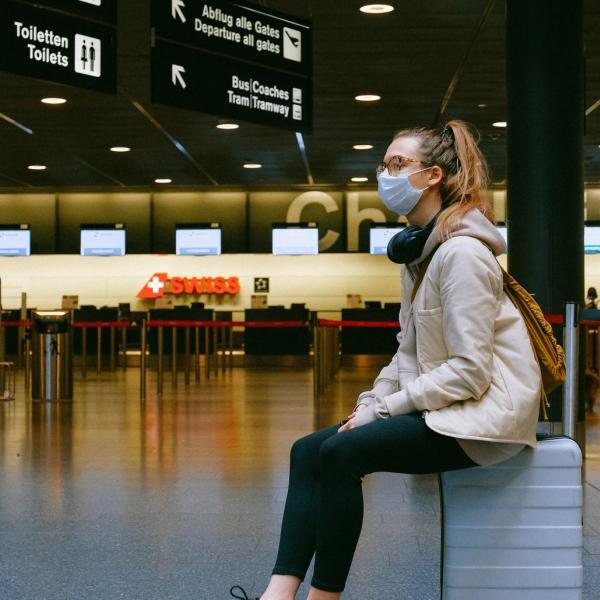 Woman sits in an airport while wearing a mask.