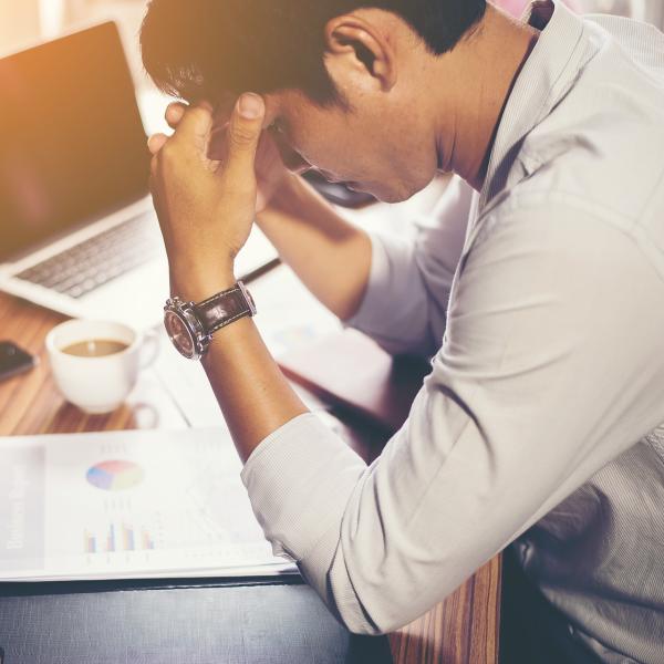 Man sitting at desk places head in hands