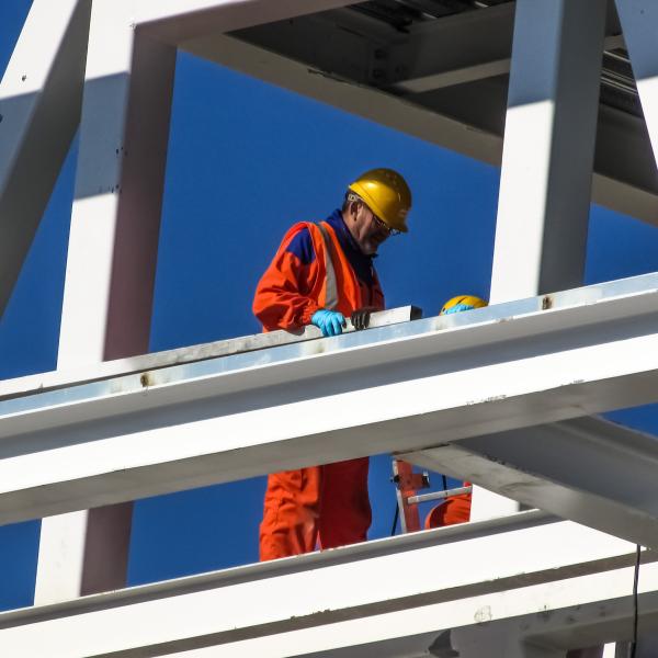 A construction worker in a helmet is seen surrounded by steel framing.