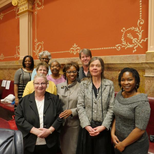 State Senator Rhonda Fields, standing next to CU faculty member Patty Limerick, and other friends and genealogists pose for a group photo in the senate chamber.