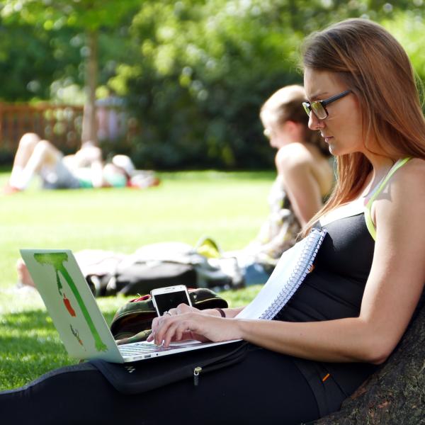Student studies sitting against tree on campus